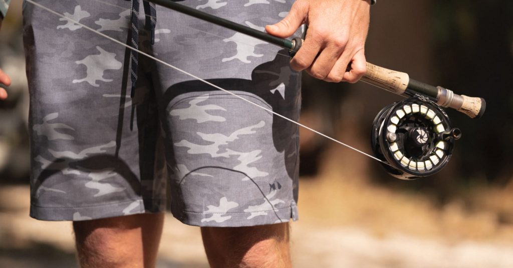 Man wearing shorts holding fly fishing rod